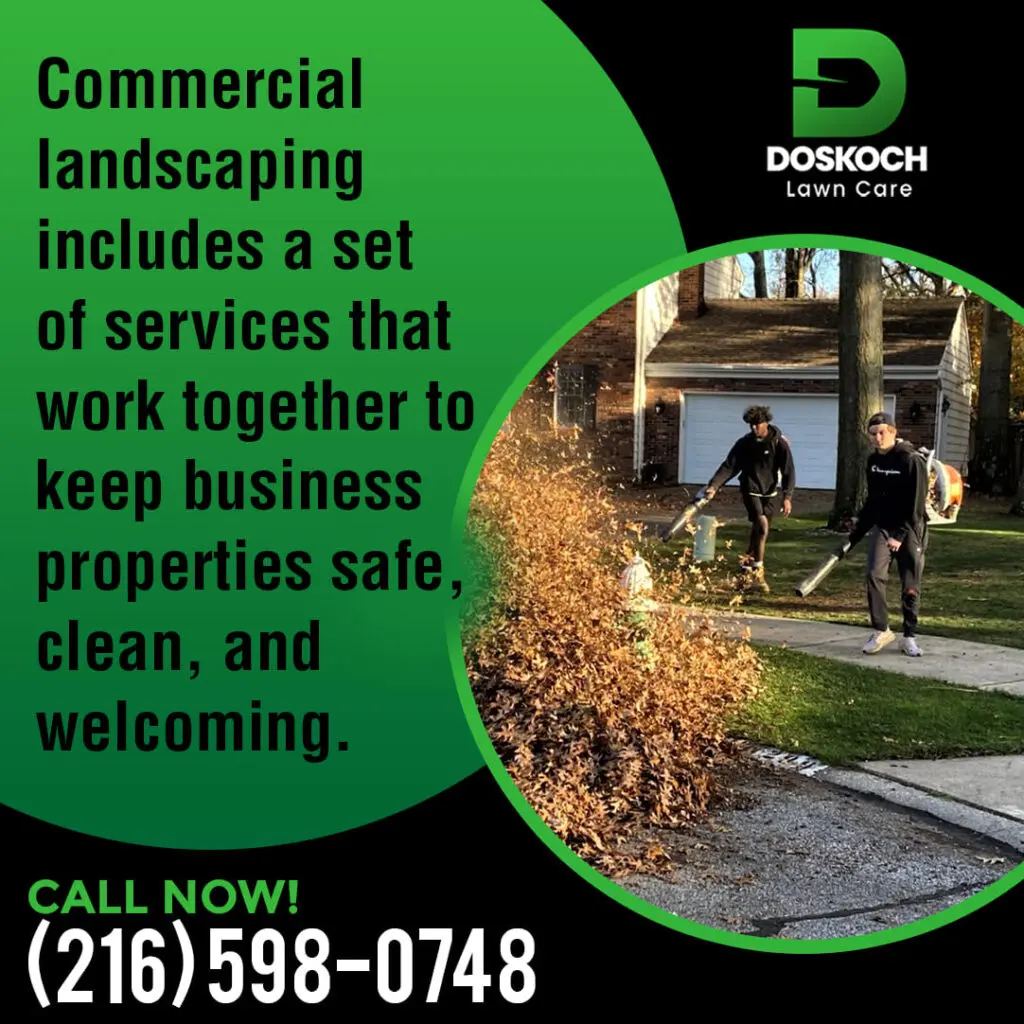 Two landscapers using leaf blowers to clear a large pile of autumn leaves from a commercial property's lawn and sidewalk