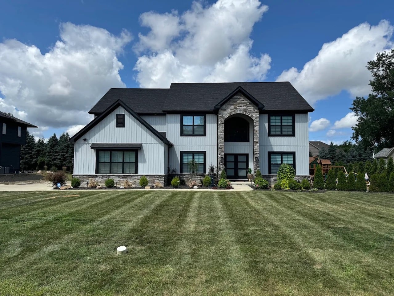 Well-maintained residential lawn with professional mowing stripes and landscaped front yard beds surrounding a modern two-story home.
