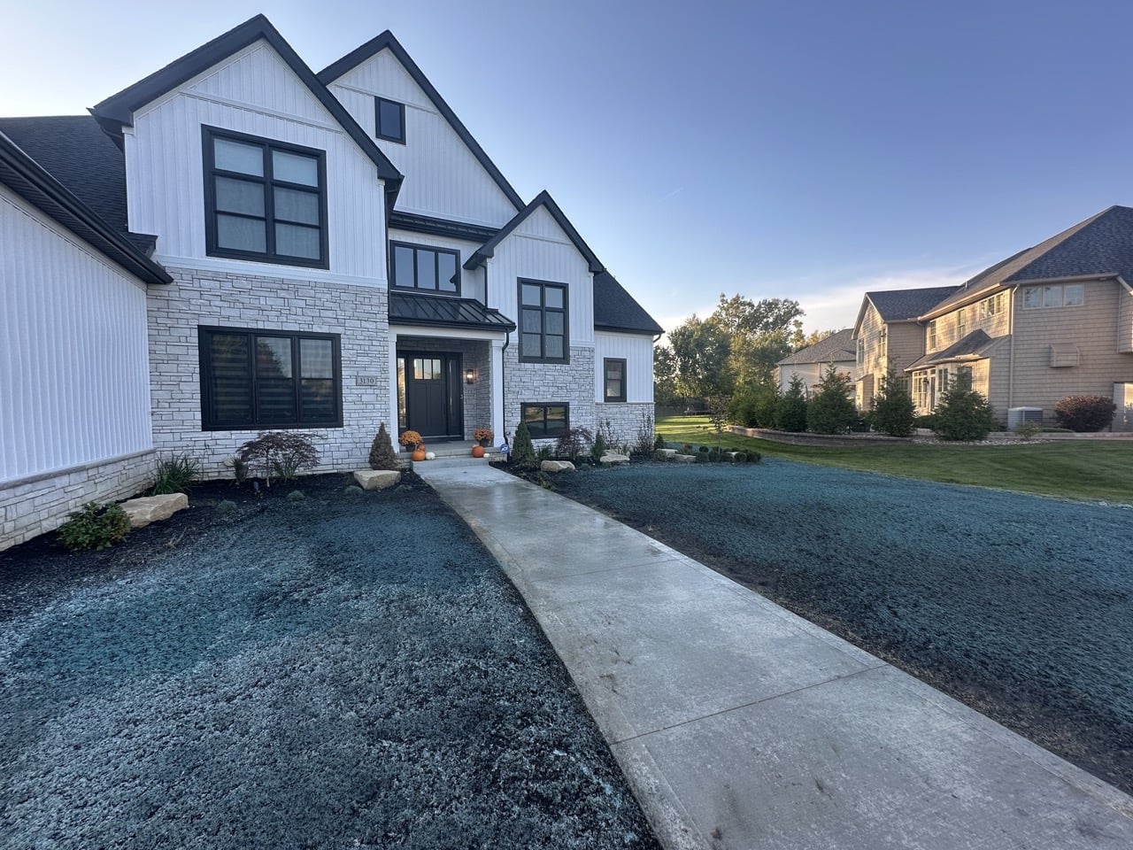 Newly installed front yard landscaping with fresh lawn treatment, clean edging, and dark mulch beds surrounding a modern white home.
