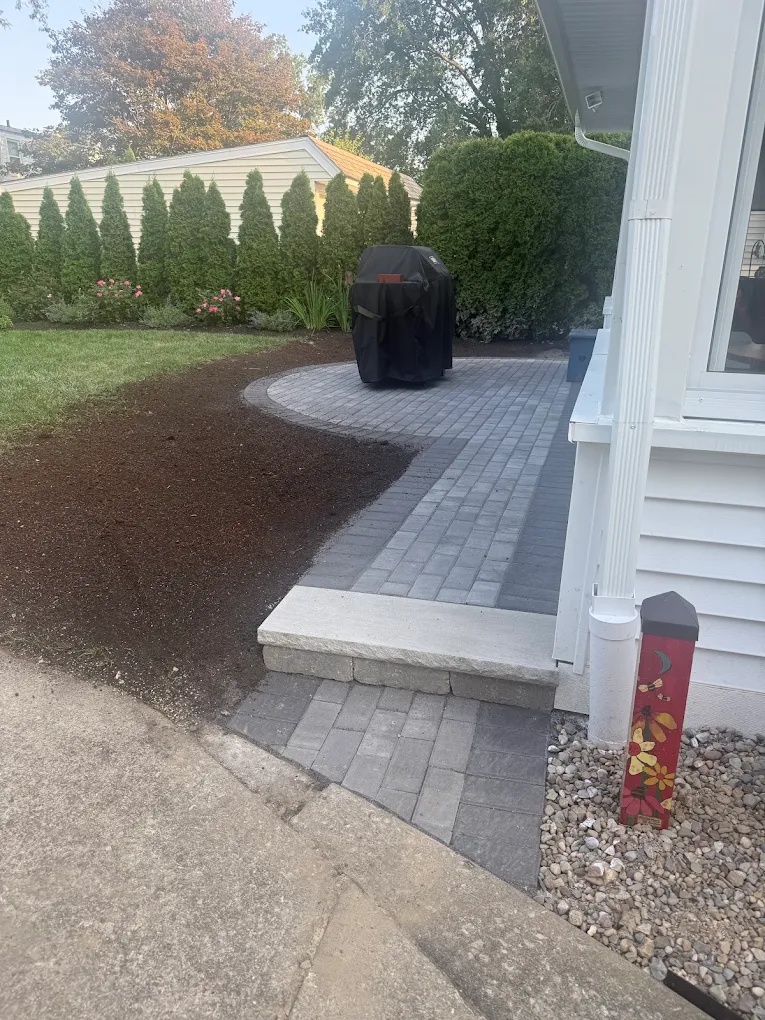 Completed gray paver patio and walkway installed beside a residential home and landscaped yard.