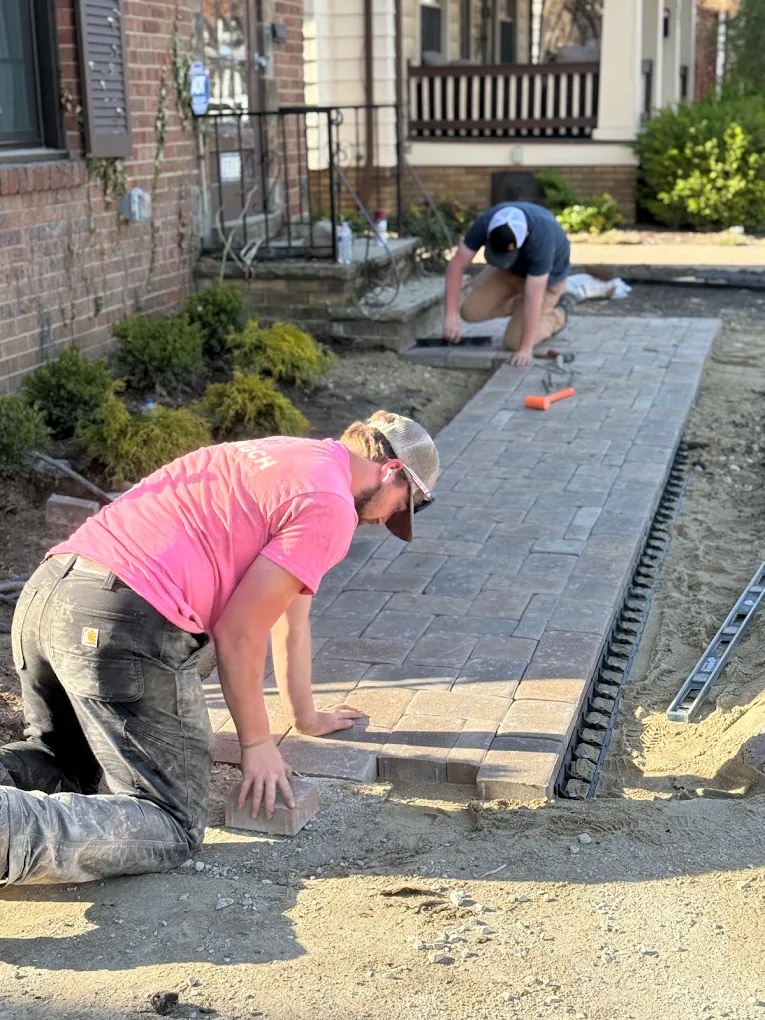 Doskoch Landscaping crew installing a gray paver walkway beside a residential home.